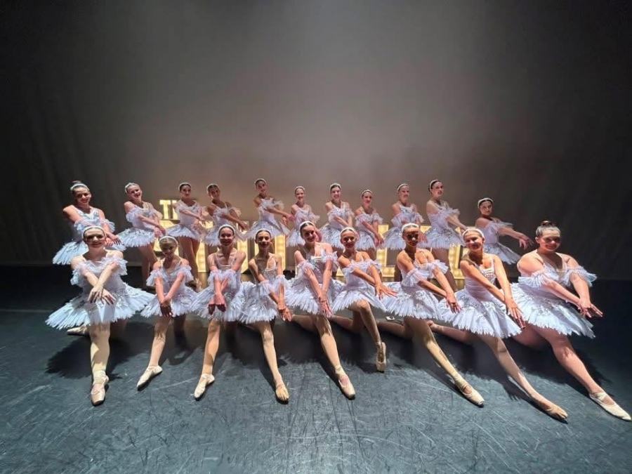 The ballet corps posed on pointe in white tutus across the recital stage