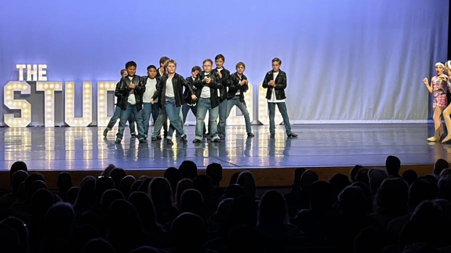 The boys crew on stage in leather jackets under the Studio marquee lights