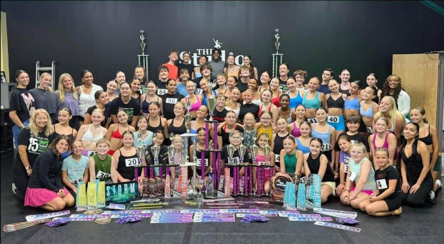 The whole competition team behind a table of trophies, banners and awards from nationals