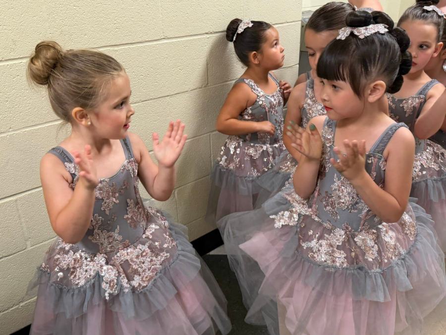 Tiny dancers backstage in sequined tutus, clapping and talking before they go on