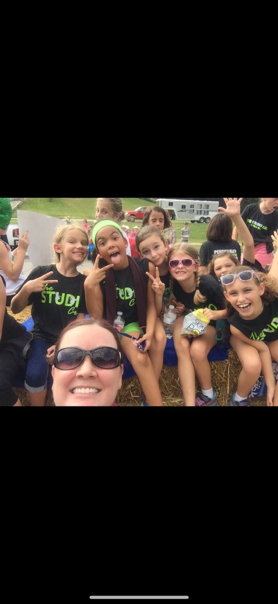 Young dancers in Studio LDG shirts on hay bales at the parade, pulling faces and throwing peace signs