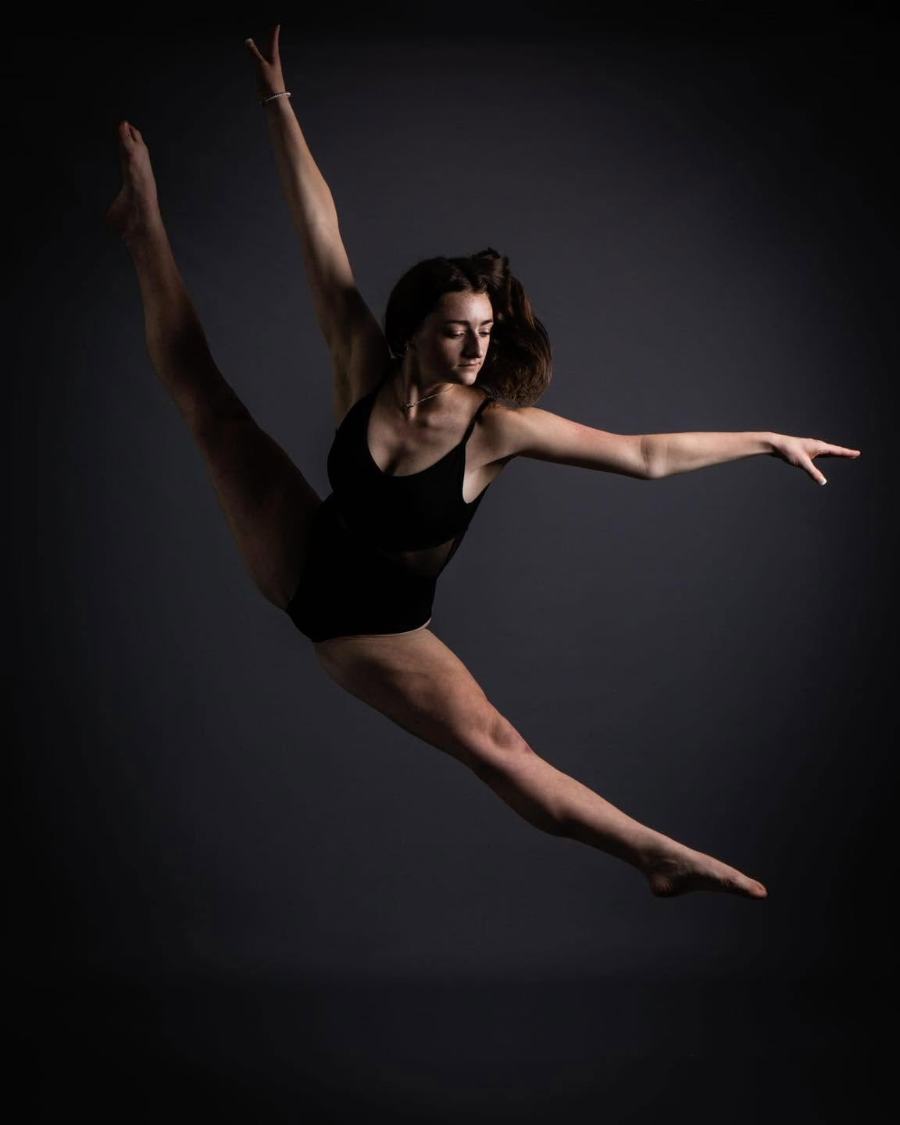 A dancer in a full split leap against a dark studio backdrop