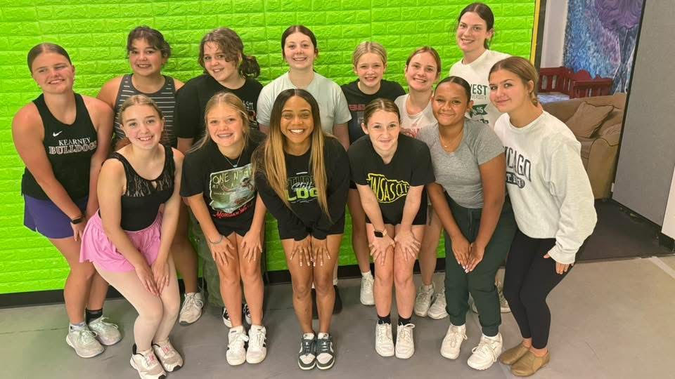 A group of teen dancers posed together against the green studio wall