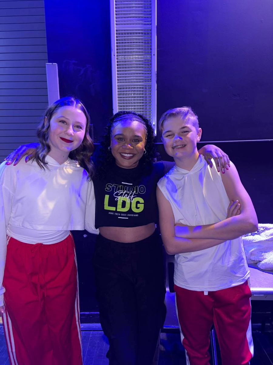 Two teen dancers backstage in costume with a member of the studio staff