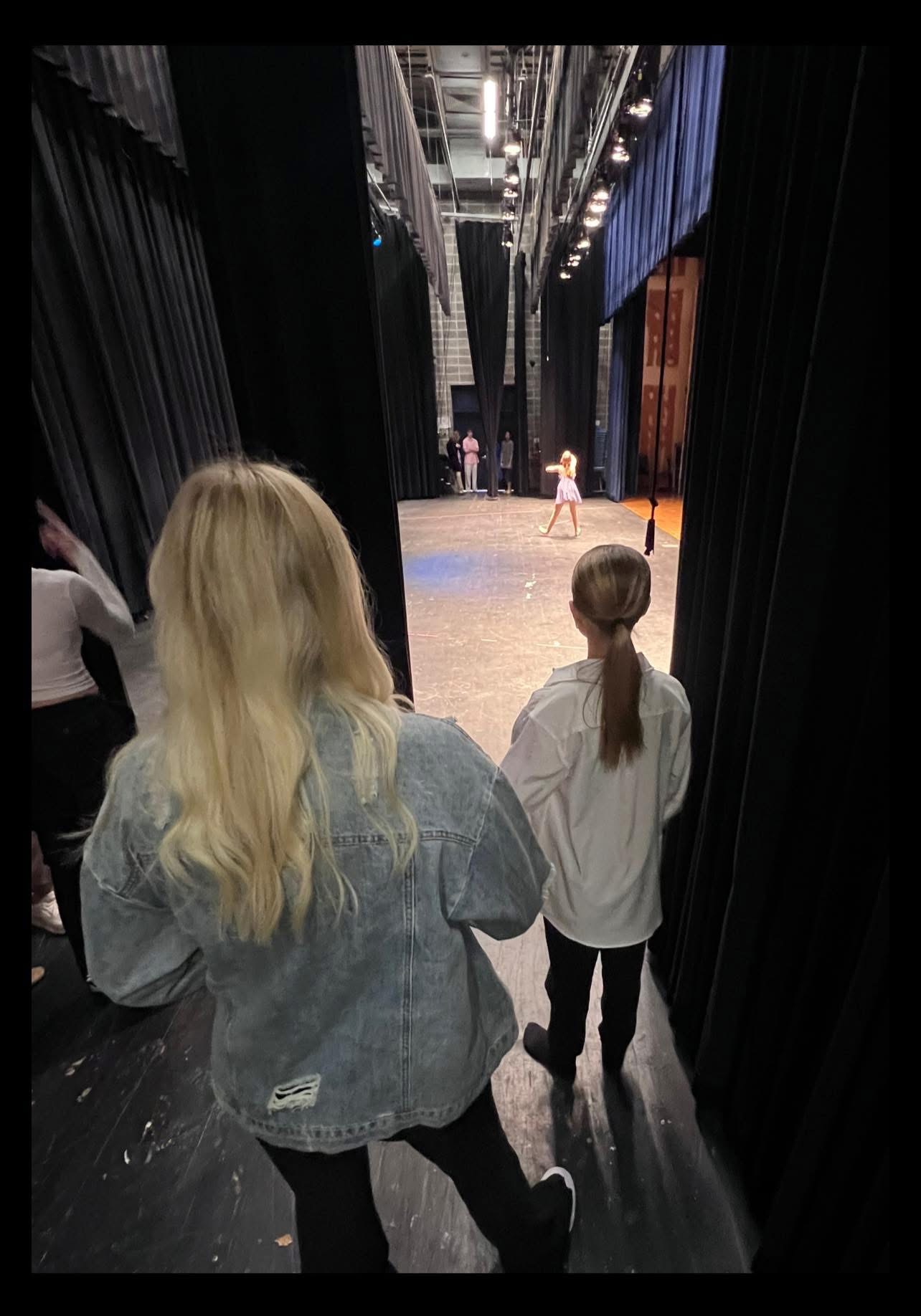 Two dancers waiting in the wings, watching another dancer out on the stage